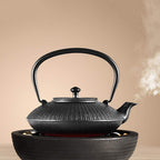 This YQBUER cast iron teapot is a 1200ml stovetop-safe Japanese tetsubin tea kettle showcasing a textured, ribbed bamboo pattern body, a short curved spout releasing steam, and an integrated overhead folding handle. The heavy-duty vintage iron tea pot sits directly atop a matching matte black cast iron warmer base with glowing internal heating elements for continuous tea temperature maintenance.