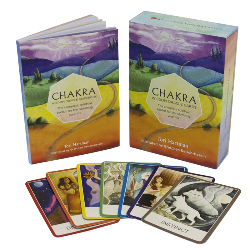 Studio shot of the Chakra Wisdom Oracle guidebook standing alongside its companion product box. Below the items, a fan of seven color-coded chakra cards rests on a plain background, with a brown-bordered card in front titled Instinct showing two white wolves under a full moon.