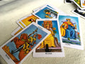 A scattered pile of traditional Rider-Waite-Smith tarot cards showcasing detailed court characters on a white surface. Visible cards include the Knight of Wands riding a rearing horse, the Queen of Wands seated on a throne with a black cat, and the King of Cups holding a golden chalice next to an open sea.