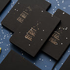 Back covers of matte black zodiac journals displaying gold constellation star maps and minimalist text descriptions for Sagittarius, Cancer, and Gemini signs.