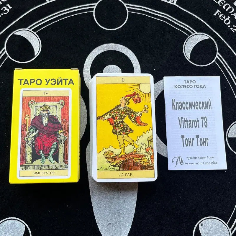 Russian Language Rider-Waite Tarot A bright yellow card box labeled "ТАРО УЭЙТА" featuring an illustration of The Emperor ("ИМПЕРАТОР") seated on a stone throne. To its right lies a deck stack topped with The Fool ("ДУРАК") under a vibrant yellow sky, alongside a small white instructional booklet printed with "Классический Vittarot 78 Тонг Тонг" on a dark cloth surface.