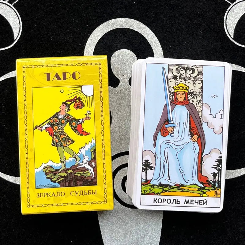 A yellow tarot card box labeled "ТАРО ЗЕРКАЛО СУДЬБЫ" in Russian next to a stack of cards on a dark, patterned altar cloth. The top card is the King of Swords ("КОРОЛЬ МЕЧЕЙ"), showing a crowned figure in a blue robe holding a raised sword.