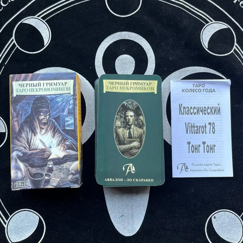 A dark, illustrative card box labeled "ЧЕРНЫЙ ГРИМУАР ТАРО НЕКРОМИКОН" with an "18+" age rating badge, showing a hooded figure writing by candlelight. To its right rests a dark green card back displaying an oval portrait of H.P. Lovecraft, alongside a white booklet titled "Классический Vittarot 78 Тонг Тонг" on a dark altar cloth.
