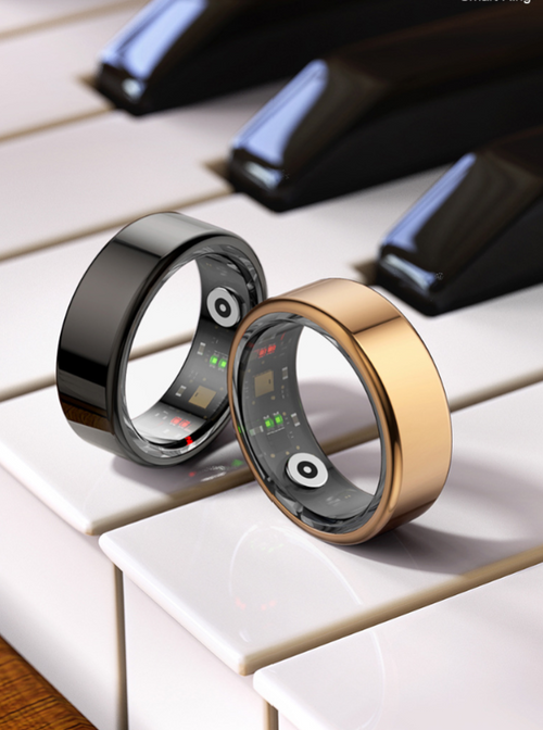A shiny black smart ring and a gold smart ring balancing on white piano keys, showing inner sensor arrays.