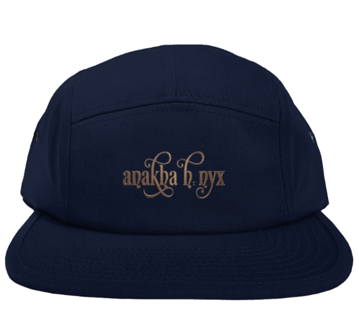 Blue five-panel camper style hat featuring the elegant Anakha H Nyx calligraphy script logo embroidered in a warm copper bronze tone across the front.