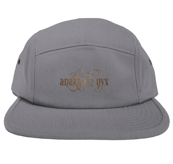 Grey five-panel camper style hat featuring the elegant Anakha H Nyx calligraphy script logo embroidered in a warm copper bronze tone across the front.