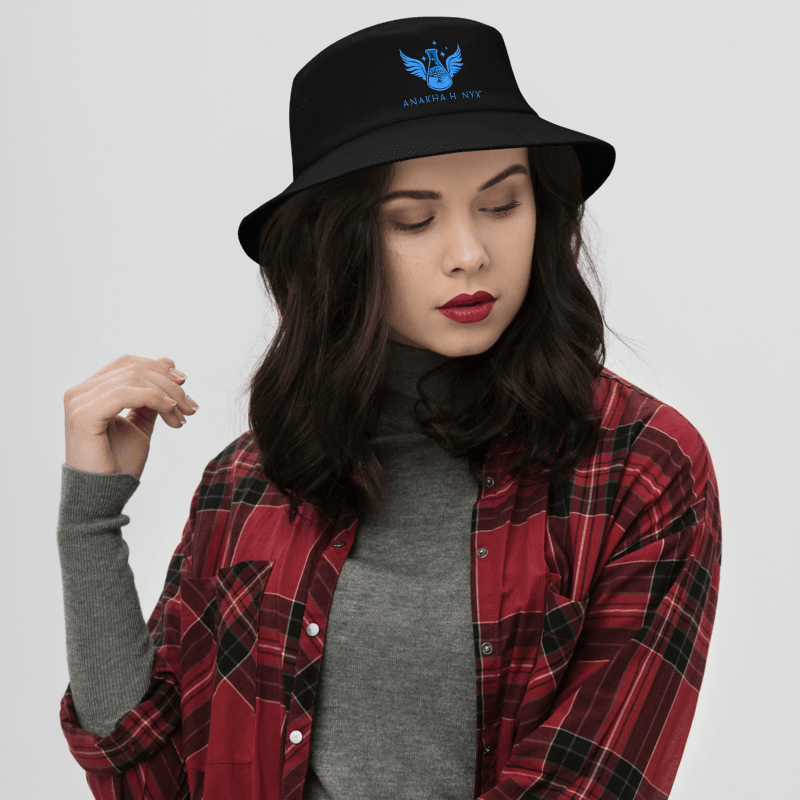 Woman wearing a black embroidered cotton twill bucket hat from Anakha H Nyx Store styled with a red flannel shirt and a gray turtleneck sweater.