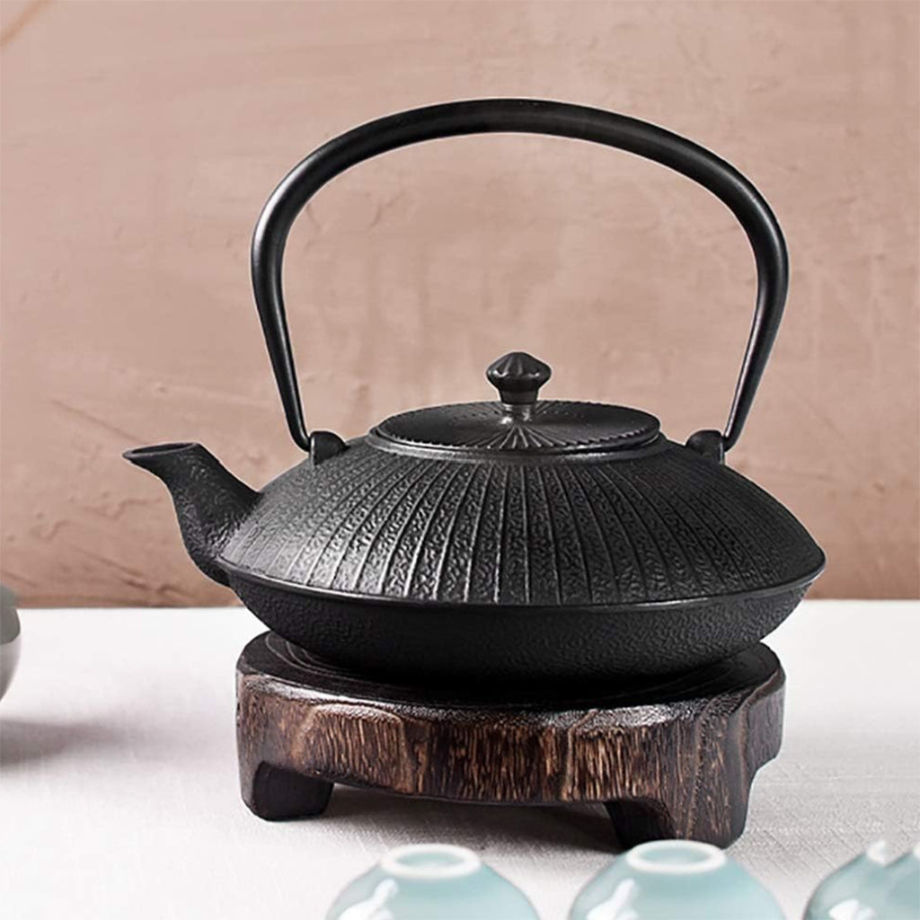 This YQBUER cast iron teapot is a 1200ml Japanese tetsubin tea kettle featuring a textured, vertical ribbed bamboo pattern exterior, curved pour spout, and a black overhead folding handle. The heavy-duty vintage iron tea pot provides maximum heat retention and rests on a matching rustic wooden trivet base for safe tabletop display during traditional tea ceremonies.