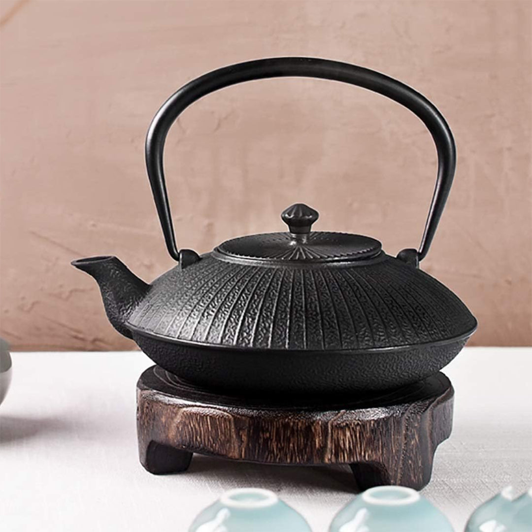 This YQBUER cast iron teapot is a 1200ml Japanese tetsubin tea kettle featuring a textured, vertical ribbed bamboo pattern exterior, curved pour spout, and a black overhead folding handle. The heavy-duty vintage iron tea pot provides maximum heat retention and rests on a matching rustic wooden trivet base for safe tabletop display during traditional tea ceremonies.