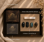 A flat-lay product infographic for the Anima Premium Crystals Protection Collection displaying its individual component pieces inside a dark wooden tray. Graphic text callouts highlight the laser-engraved square wooden box, the raw selenite charging stick, the four raw crystals including obsidian and black tourmaline, and the included protection collection guide leaflet.