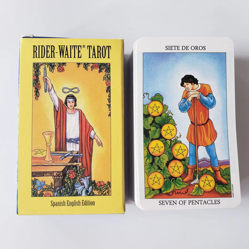 The yellow Spanish-English edition box next to the Seven of Pentacles tarot card displaying a man leaning on a shovel.
