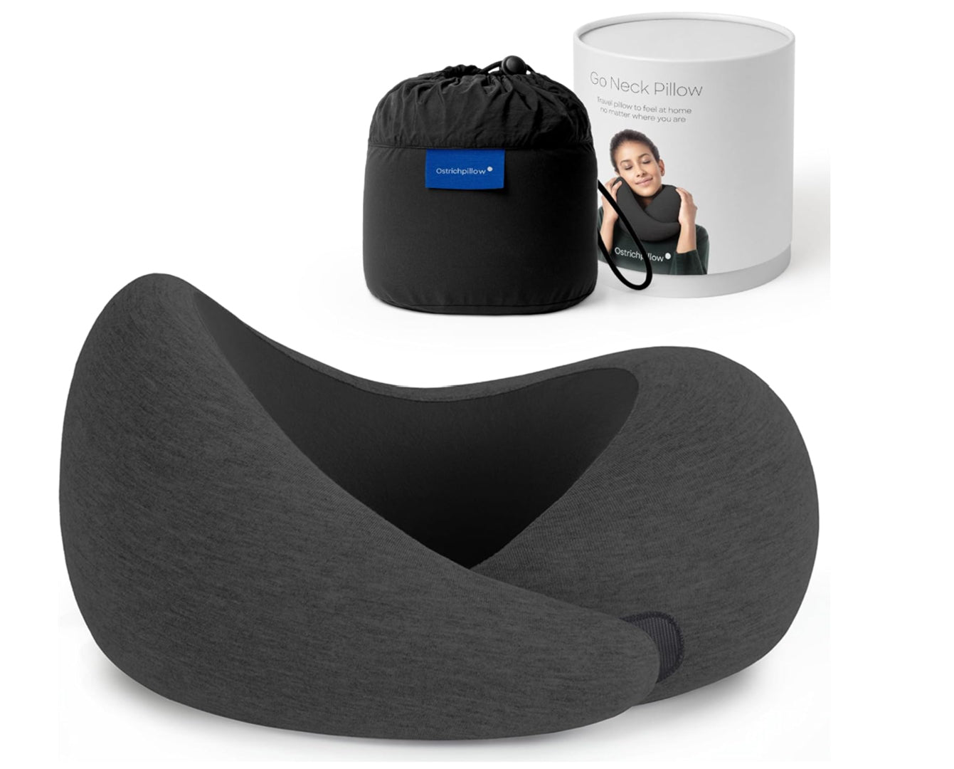 Travel memory foam neck pillow from the Dark Utility Collection in charcoal black with a black interior lining, heather knit modal-blend cover, asymmetrical ergonomic wrap construction, hook-and-loop closure, and black compression storage bag beside branded packaging. 