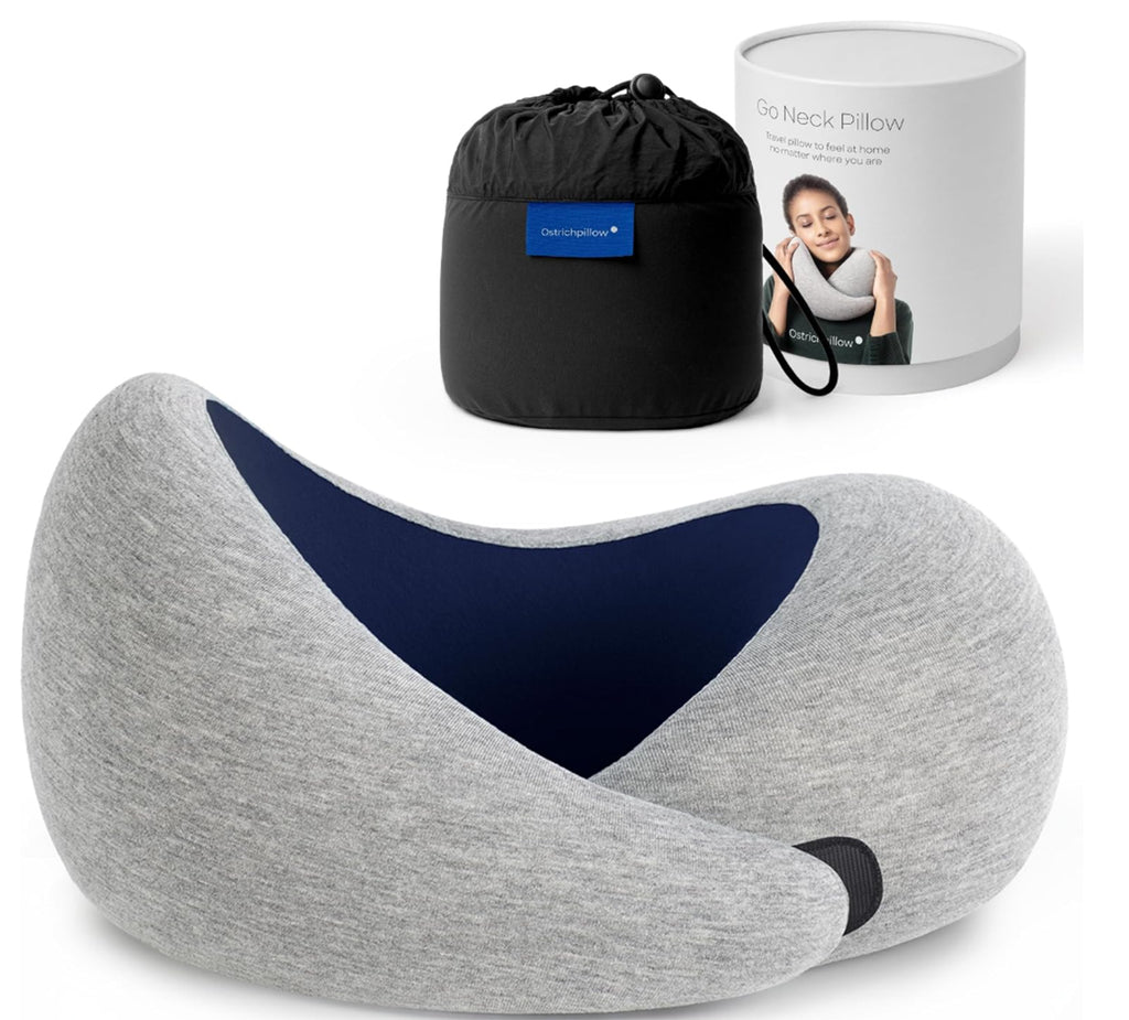 Travel memory foam neck pillow from the Dark Utility Collection in heather gray with a navy interior lining, modal-blend knit exterior, asymmetrical ergonomic profile, hook-and-loop closure, and black compression storage bag displayed beside branded packaging. Product image focuses on textured fabric, supportive memory foam construction, utility detailing, and understated styling for dark streetwear, minimalist gothic apparel, corporate goth, and travel gear.