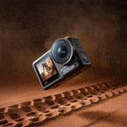 This premium lifestyle asset depicts the DJI Osmo Action 4 waterproof 4K action camera dynamically suspended over a deep tire track on a sandy desert trail. The high-impact promotional shot highlights the device's extreme dustproof and shock-resistant structural engineering, with real-time dirt debris explosions framing the main unit's dual full-color displays and f/2.8 ultra-wide lens.