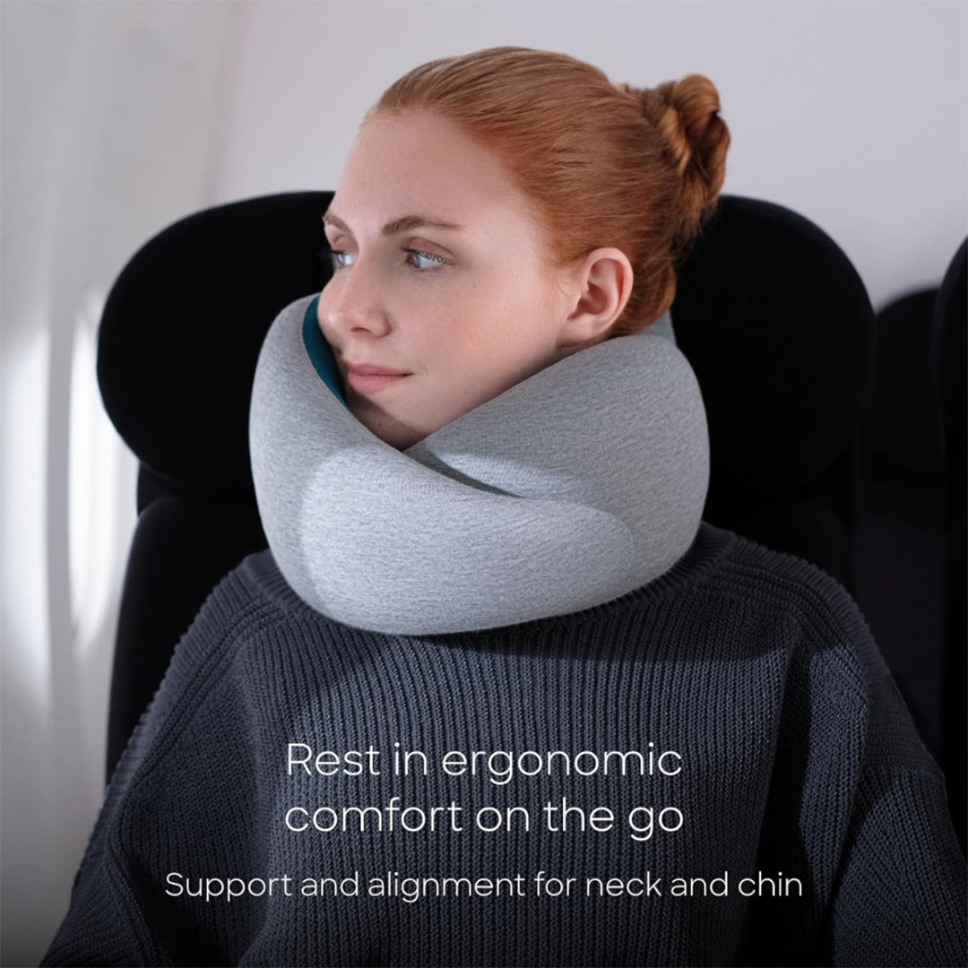 Travel neck pillow from the Dark Luxury Travel Collection with soft modal-blend fabric, ergonomic memory foam support, wraparound chin and neck alignment, light gray knit texture, and adjustable hook-and-loop closure shown during seated travel.