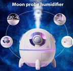 An infographic display of the TOPINCN moon probe spaceship humidifier highlighting its structural components against a starry galaxy backdrop. Four circular graphic callouts demonstrate the 220ml water tank capacity, the open hatch door, the astronaut capsule visor, and the rear USB power port.