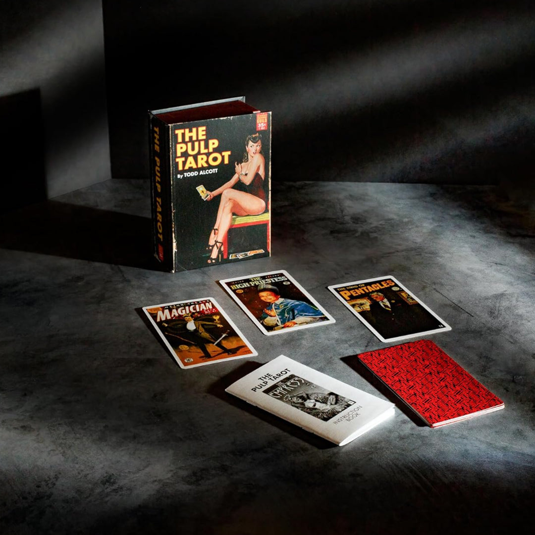 The Pulp Tarot lifestyle flatlay presents the full 78-card divination deck arranged beneath dramatic studio shadow lighting on a textured surface. The promotional product spread features the book-style magnetic box standing upright alongside individual illustrated cards like The Magician, The High Priestess, and The King of Pentacles, positioned next to the instruction guidebook and patterned card back.