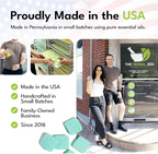 A brand overview graphic titled "Proudly Made in the USA" showcasing production behind-the-scenes, a family-owned business team standing outside a glass storefront door, and several green square shower steamer tablets scattered at the bottom.